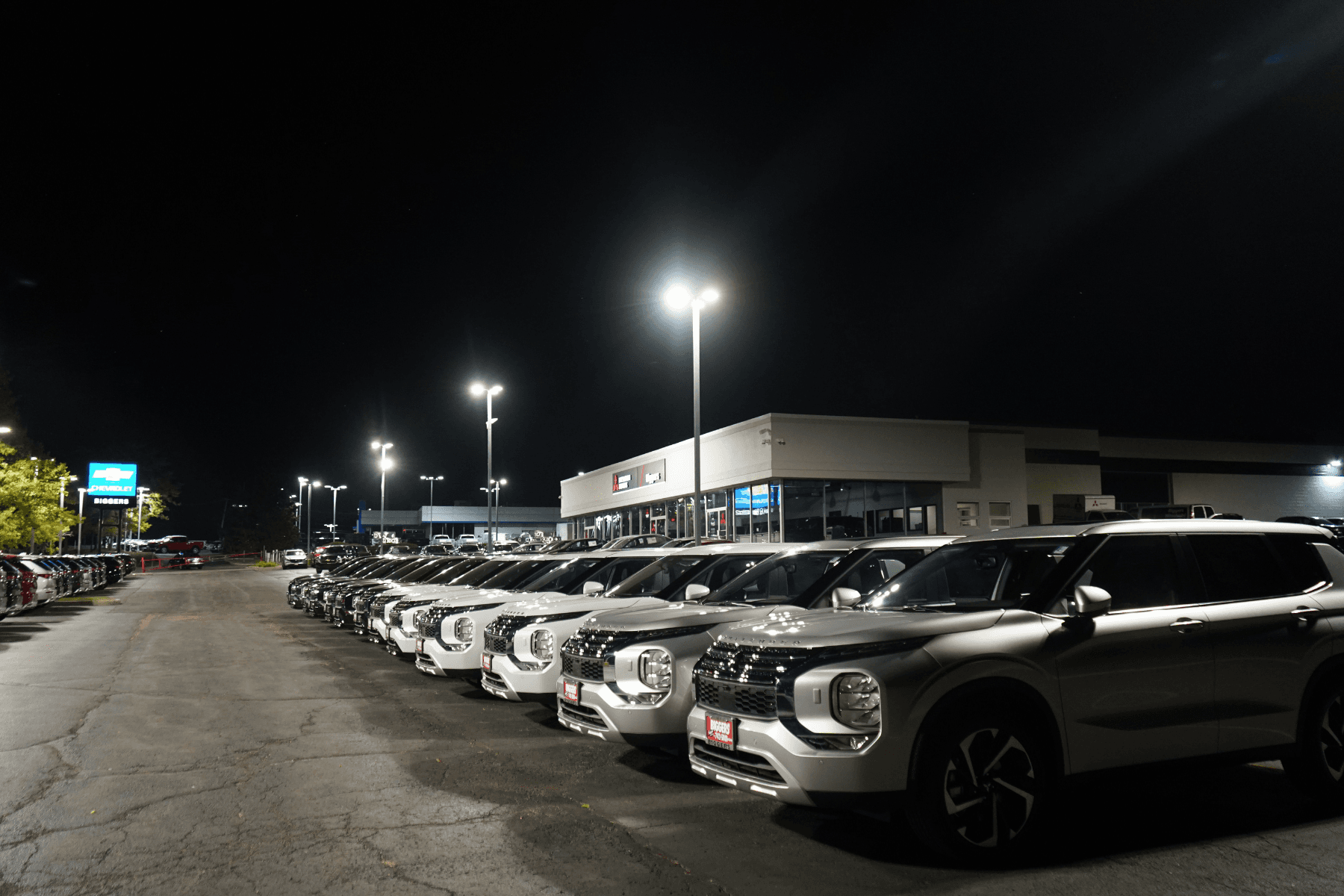 Auto dealership parking lot illuminated by exterior pole lighting at night